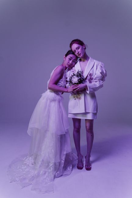 A delicate floral gift featuring a bridal bouquet of white and purple flowers, including roses and greenery, arranged with a combination of fresh petals and stems. The bouquet is wrapped in transparen